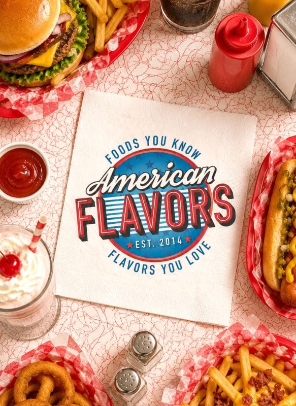 Top-down mockup of the American Flavors logo printed on a diner napkin surrounded by burgers, fries, hot dogs, onion rings, and milkshakes.